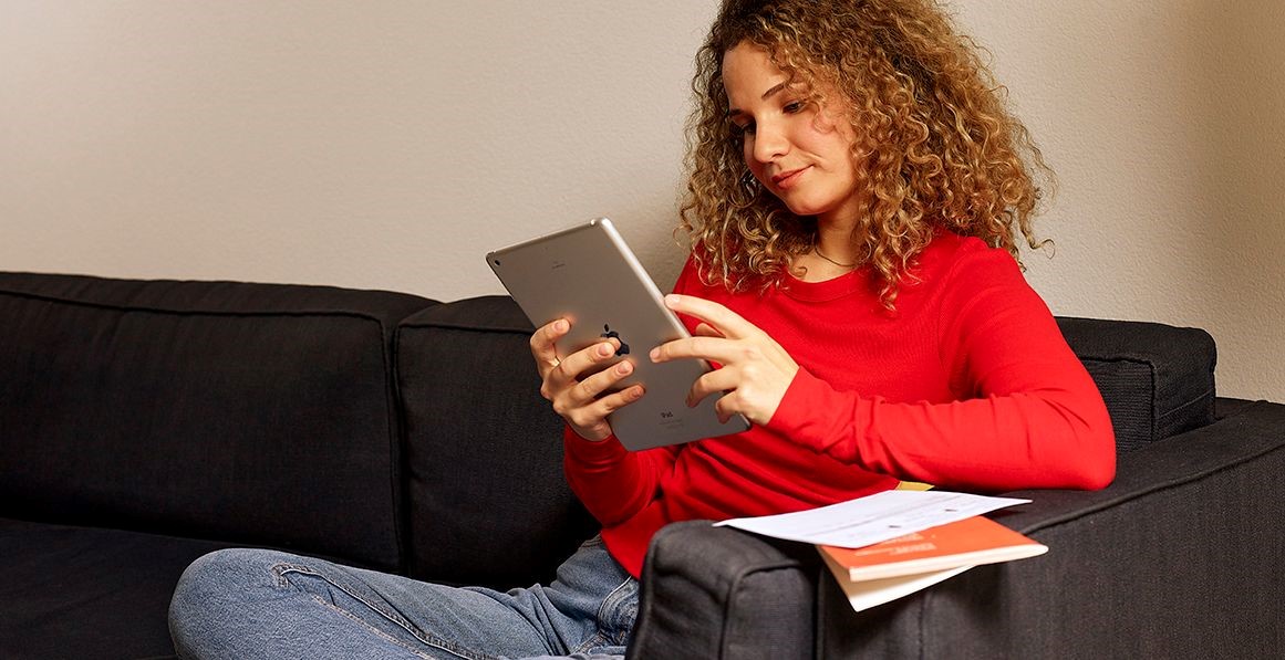 Eine junge Frau nutzt konzentriert ihr Tablet für eine digitale Abstimmung; neben ihr liegen physische Abstimmungsunterlagen als Symbol für den Wandel zum E-Voting.