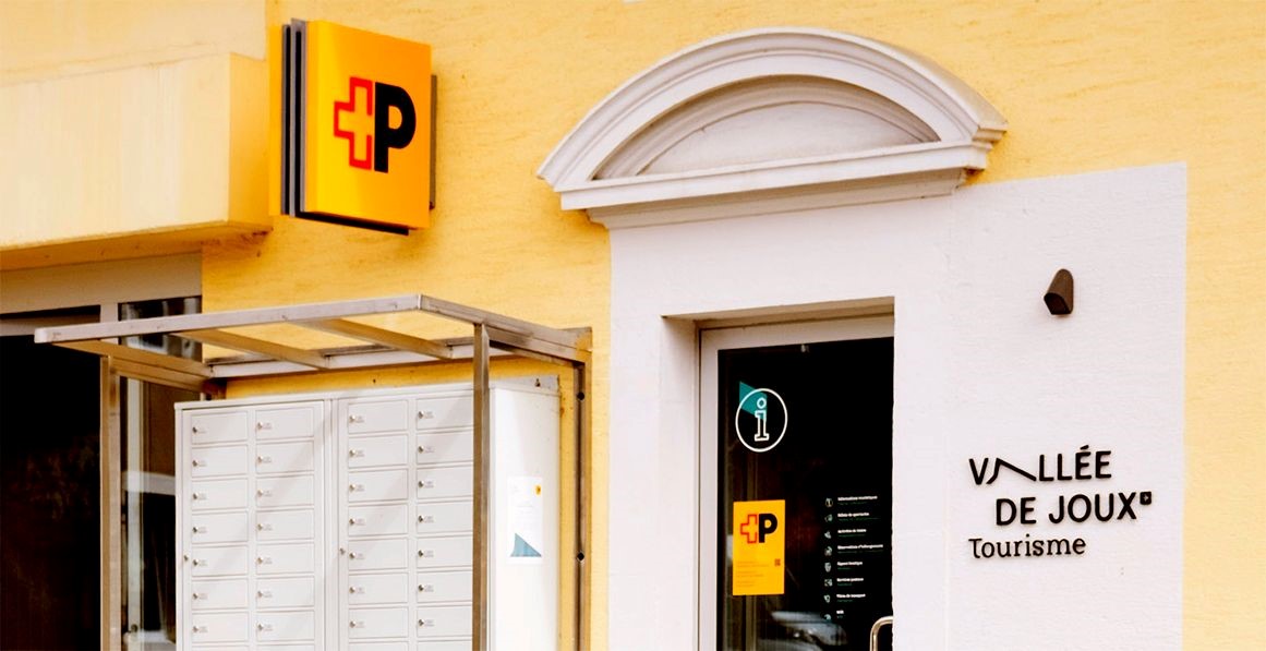Aussenansicht einer Kooperationsfiliale: Neben einer Postfachanlage befindet sich der Eingang zum Tourismusbüro Vall.e de Joux, an dessen Tür ein Post-Logo auf die integrierten Postdienstleistungen hinweist.