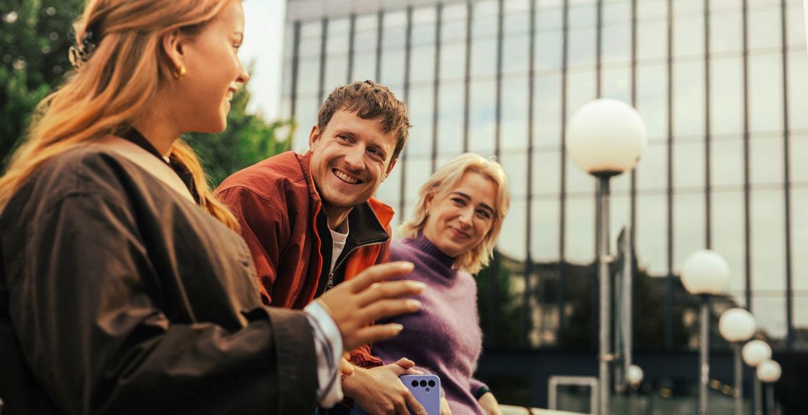 Drei junge Erwachsene unterhalten sich lächelnd im Freien vor einem modernen Bürogebäude.
