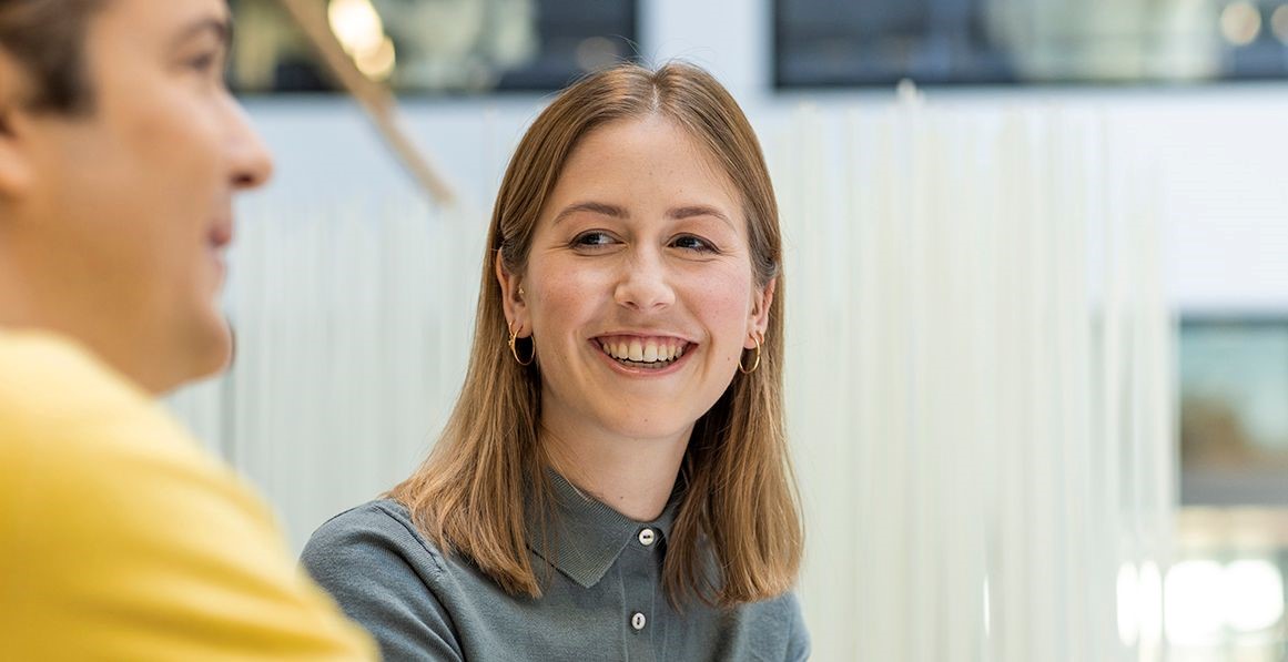 Porträtaufnahme einer lächelnden jungen Mitarbeiterin der Post in einem hellen, modernen Büroumfeld.