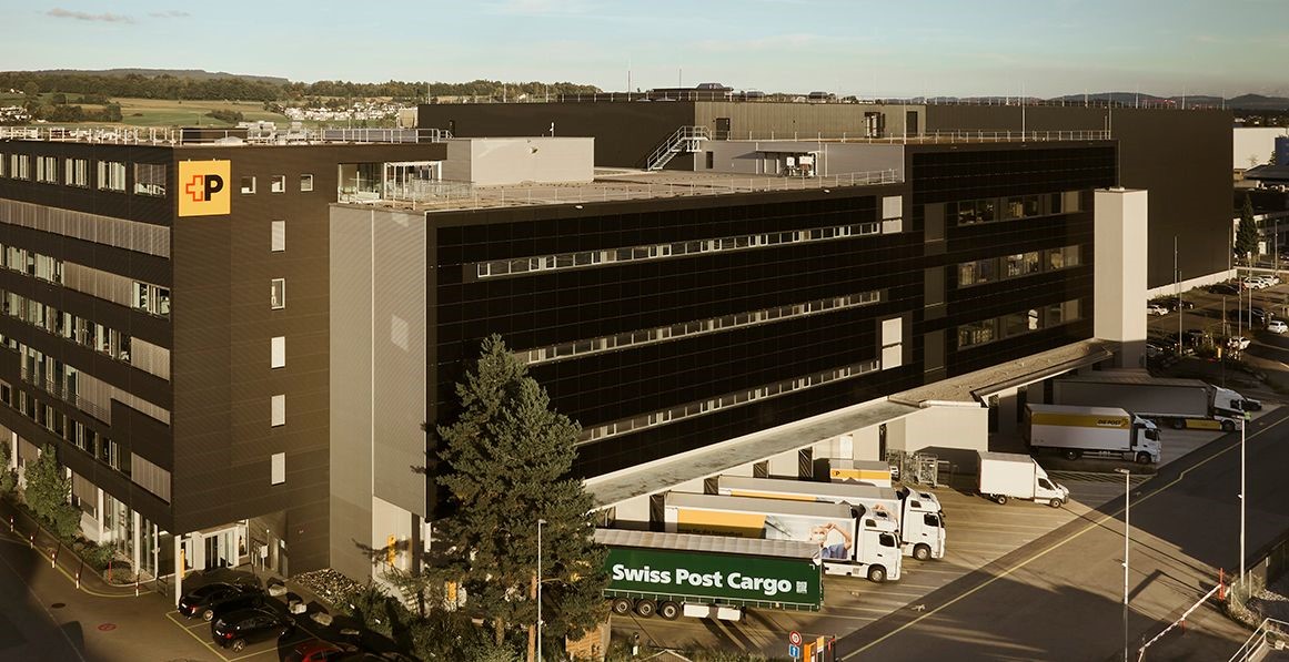Grosse Aussenansicht des modernen Lagerlogistikzentrums der Schweizer Post in Villmergen mit mehreren LKW-Andockstationen.